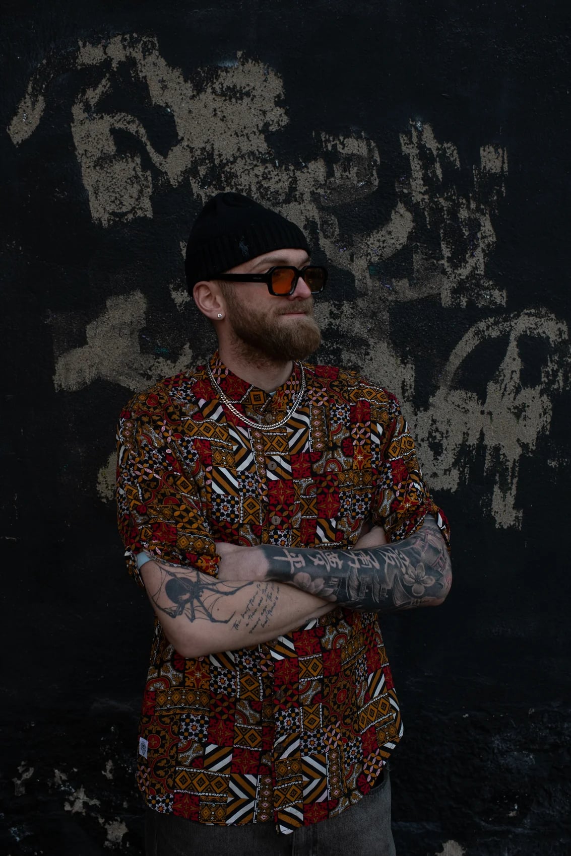 Man in a 2CC printed short-sleeve shirt against a dark wall