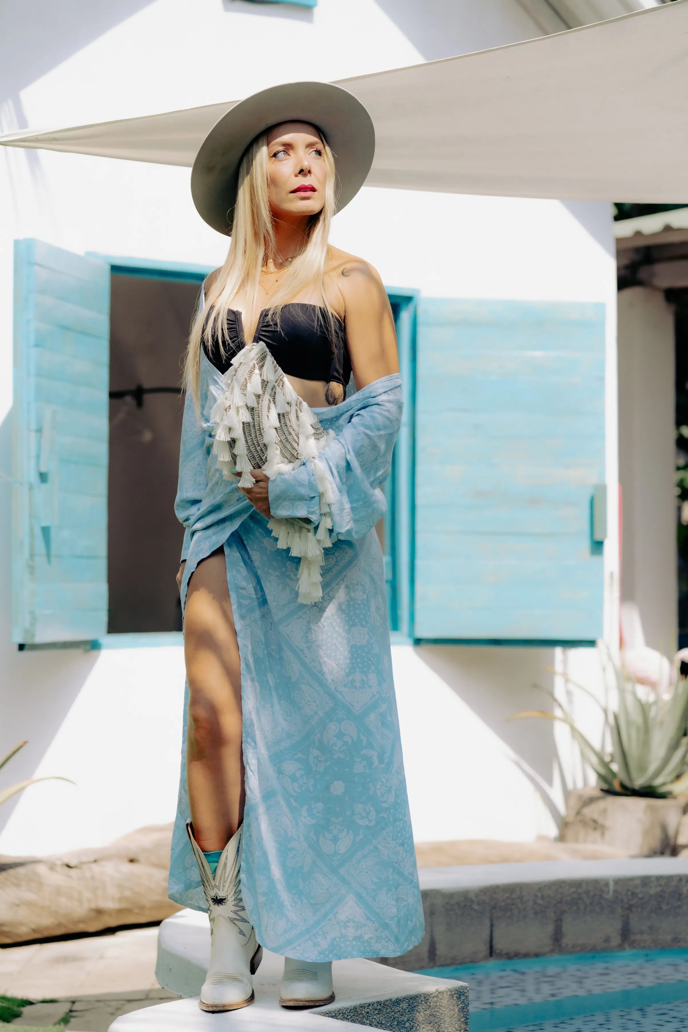 Woman in a wide-brimmed hat and a long pale-blue 2CC kimono in front of turquoise shutters